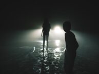 silhouettes of two people standing on the background of car lights at night